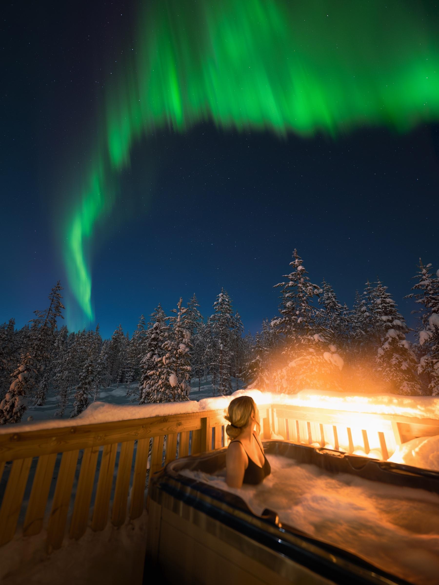 Michelle filming from the bed of a glass igloo under the aurora